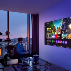 Mężczyzna gra na konsoli, a jego pies siedzi obok. Na ekranie telewizora widać gry, idealne do wyboru między oled czy qled.