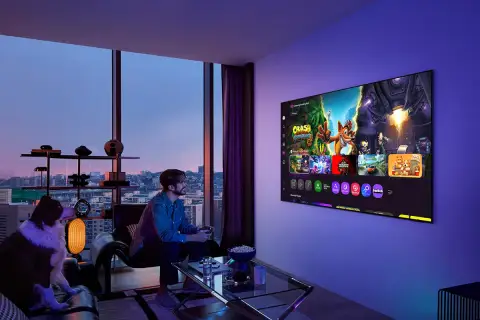 Mężczyzna gra na konsoli, a jego pies siedzi obok. Na ekranie telewizora widać gry, idealne do wyboru między oled czy qled.