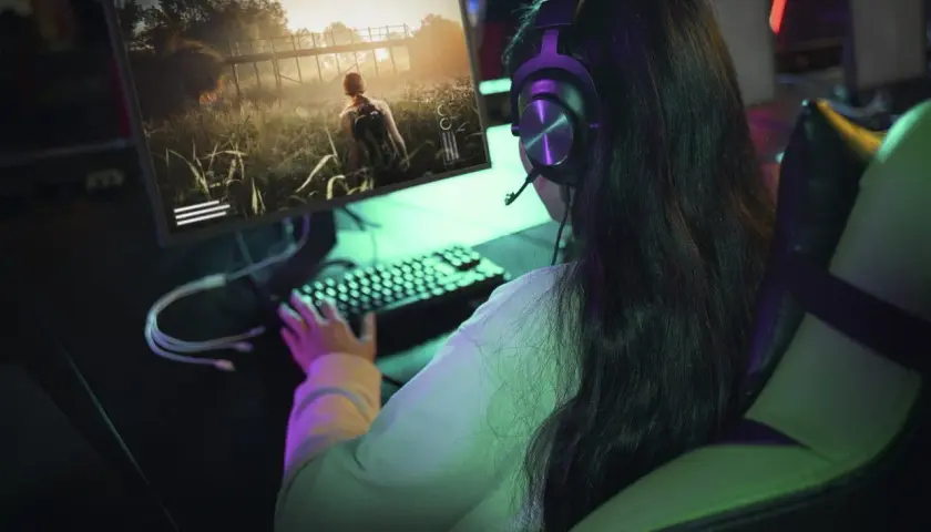 Dziewczyna w słuchawkach gra w grę fps na komputerze. Wirtualna przygoda wciąga ją bez reszty.