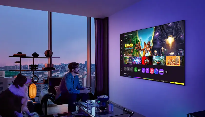 Mężczyzna gra na konsoli, a jego pies siedzi obok. Na ekranie telewizora widać gry, idealne do wyboru między oled czy qled.