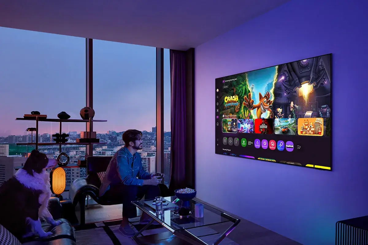 Mężczyzna gra na konsoli, a jego pies siedzi obok. Na ekranie telewizora widać gry, idealne do wyboru między oled czy qled.