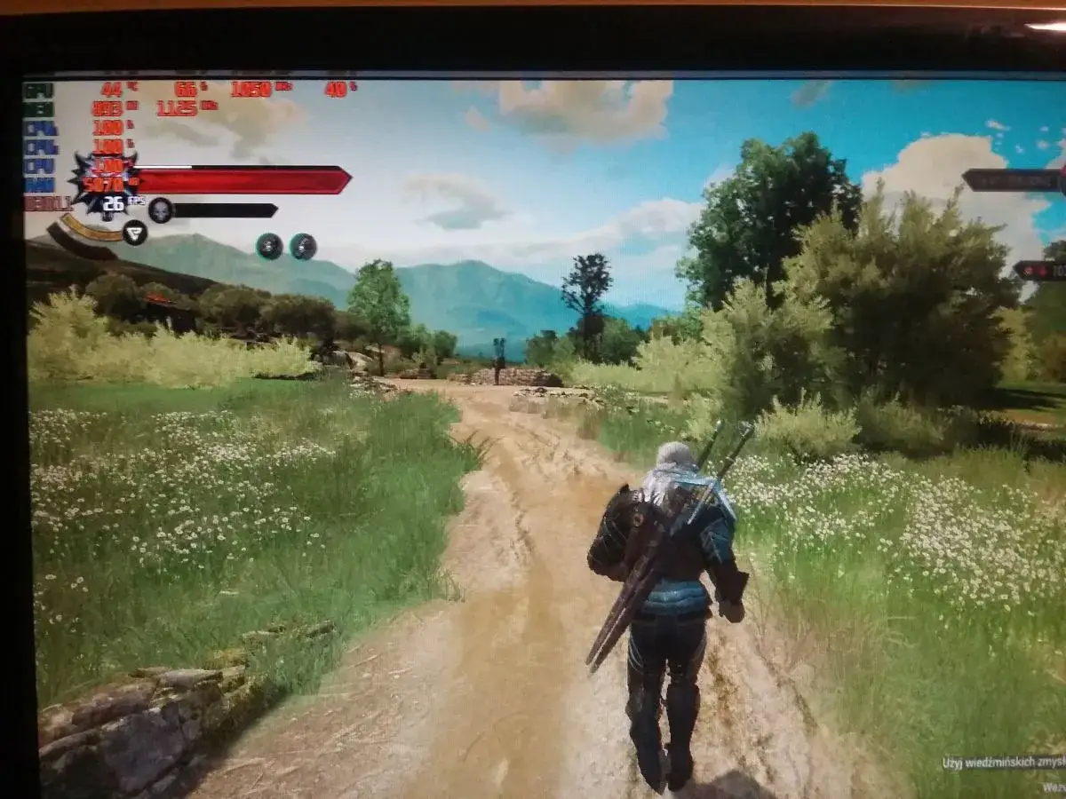 Geralt idzie polną drogą, a na ekranie widać wskaźniki wydajności, sugerujące throttling.